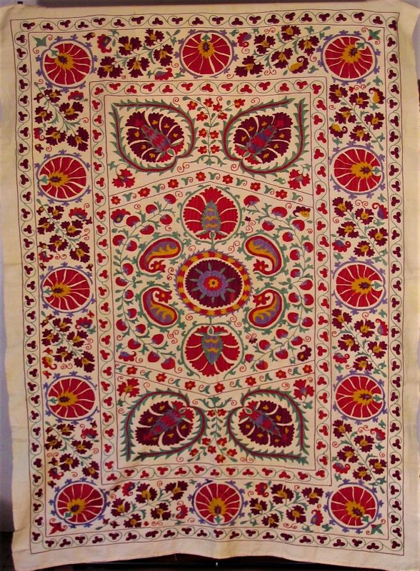 DESCRIPTION: A vibrant Suzani coverlet, finely embroidered with silk threads on a cream-colored cotton ground.  Suzani (a word meaning “needlework”) is a type of embroidered tribal textile made in Uzbekistan, Kazakhstan and other Central Asian countries.  These coverlets are traditionally made by Central Asian brides for their dowry and presented to the groom on the wedding day.
<p>This vintage suzani was acquired in Turkey from an Uzbek family and displays traditional design motifs such as sun and moon disks, flowers, leaves, vines and pomegranates.  Excellent condition; no damage or stains.  DIMENSIONS: 84.5” x 60.5”  
<div id='rater_target1362784'></div>
