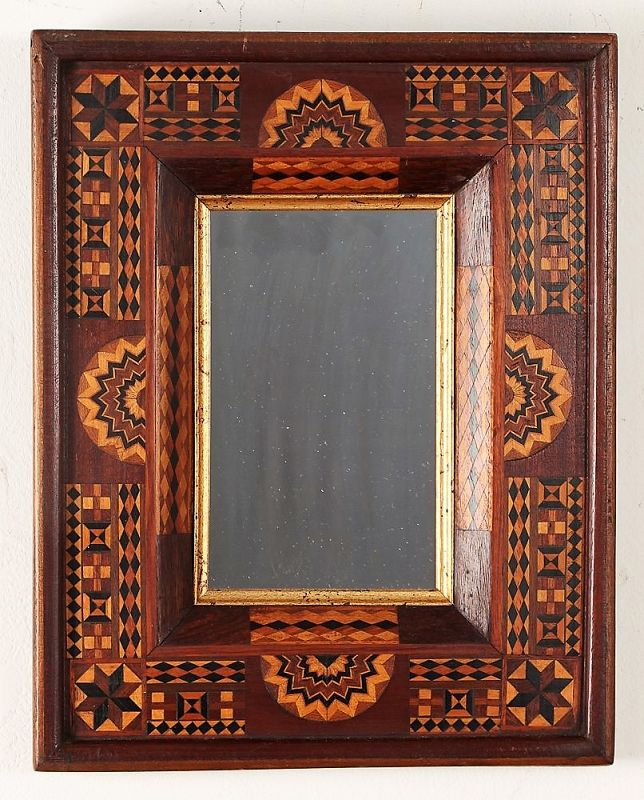 DESCRIPTION: A fine antique folk art frame with deeply set mirror, the frame intricately inlaid with multi-colored woods forming geometric designs including diamonds, stars, fans and other parquetry motifs. This is a wonderful folk art piece executed with obvious skill; narrow beaded inner frame is gold leaf. Excellent condition, no losses or cracks. Provenance: Clifford A. Wallach, Tramp Art, Folk & Americana.  DIMENSIONS: 13 5/8” high x 11” wide. 
<div id='rater_target1365598'></div>
