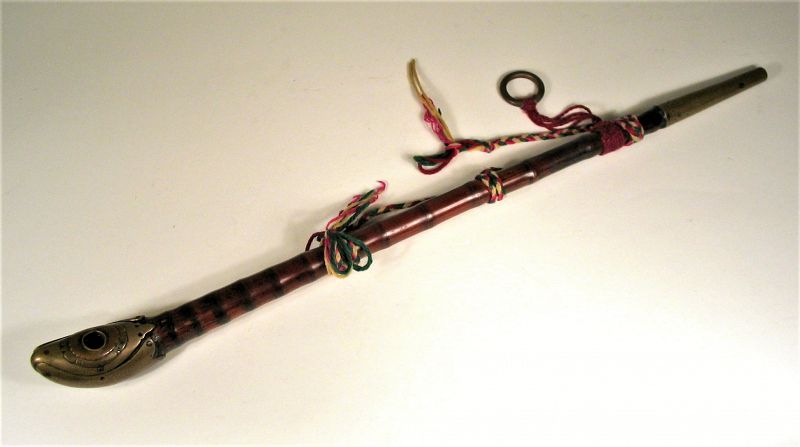 DESCRIPTION: A large, non-damper opium pipe, consisting of a long bamboo tube terminating at one end with a bowl of brass and copper overlay acting as the saddle, socket and damper.  A  tapering brass tip finishes the other end. Around the bowl is a double flower design in copper and brass, and on each side is a decorative brass fish with scales. Attached along the bamboo stem are lengths of braded yarn, one of which terminates in a brass ring for hanging. Purchased from the collection of Jean-Philippe Weber, a French ex-pat living in Shanghai, and shown on p. 13 in the book “China Style” (see photo included), by Sharon Leece, published by Periplus Editions, 2002. DIMENSIONS: 19 ½” long (49.5 cm).   
<div id='rater_target1367465'></div>
