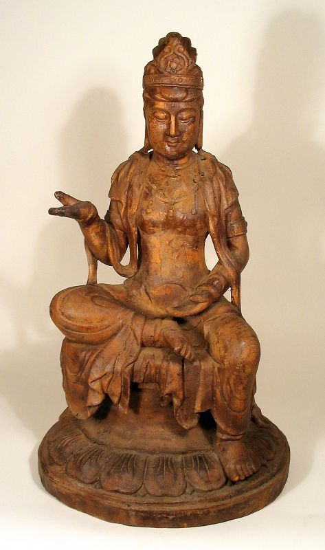 DESCRIPTION: A large, carved wood figure of the Chinese deity Guanyin (also Quanyin, or Kwan-yin), seated on a throne with right leg folded and right hand extended in the abhaya mudra position, a gesture of reassurance, blessing and protection (or “do not fear”). Her hair is worn pulled up in a chignon inside her crown, and around her shoulders is draped a short shawl with flowing ribbons. In good, solid condition with minor age wear; early 20th C.  DIMENSIONS: 24 ½” high (62 cm) x 14” wide at the base (35.5 cm). 

<p>CULTURAL BACKGROUND: Guanyin is the Chinese deity of compassion and mercy. She is one of the most favored and well known of the Bodhisattvas, enlightened beings who have delayed entering paradise in order to help others attain enlightenment. In the Chinese language, "Guanyin" means "observing the sounds," meaning Guanyin hears all the sounds from the world and listens to the prayers from her worshippers. This goddess comforts the troubled, the sick, the lost, and grants sons to the infertile.   

<div id='rater_target1371701'></div>
