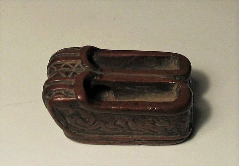DESCRIPTION:  An antique Chinese boxwood toggle (Guajian) carved as a pair of men’s shoes resting side by side, a symbol of marital harmony and the wish for many sons.  The shoes are elaborately carved with hollowed interior, relief banding, and incised designs on all sides including the soles.  A hole running through the inner sides of each shoe forms the track used for threading cords from which this toggle would have been suspended as a counterweight to some other object.  An outstanding example of Chinese folk art dating from the 19th C. (Qing Dynasty), this toggle is in overall fine condition with normal signs of wear and usage, the fine-grained boxwood having a wonderful, aged patina from years of use.  DIMENSIONS:   2” long (5 cm) x .75” high (2 cm).
<div id='rater_target1371999'></div>
