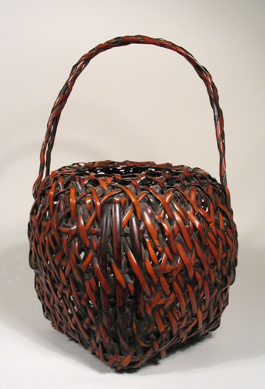 DESCRIPTION: A handsome ikebana basket, Meiji Period, crafted of smoked bamboo in a diagonal weave with double wrapped handle. Three vertical bamboo strips reinforce two corners, and the basket rests on a square, open weave base. Excellent condition with no breaks or losses. Ikebana ("living flowers") is the Japanese art of flower arrangement. It is also known as Kado ("way of flowers"). Japanese artists crafted Beautiful baskets such as this one as containers to hold simple to elaborate ikebana arrangements. DIMENSIONS: 16 ½” high with handle (42 cm); 10 ½” diameter (26.5 cm).   
<div id='rater_target1373569'></div>
