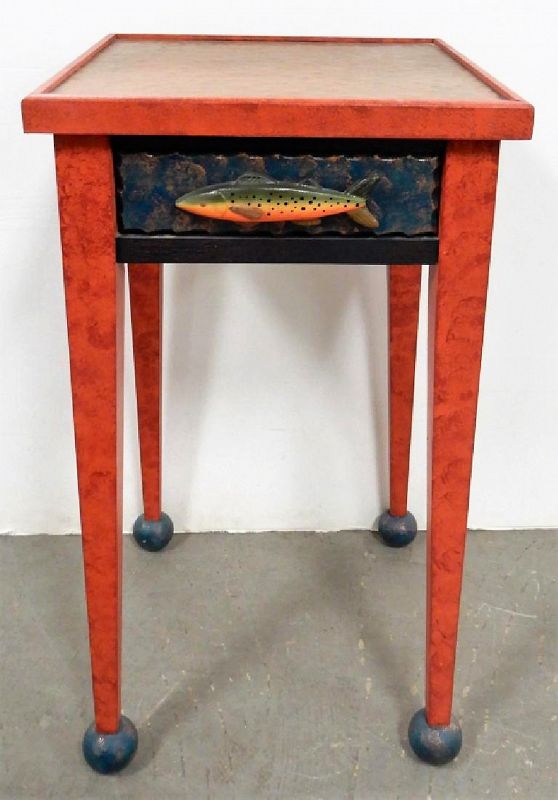 DESCRIPTION: A delightful contemporary folk art table by craftsman, Richard DeWalt, in which vermilion colored tapering legs with small ball feet rise to support a copper table top. The sides and front drawer are finished in blue with a charming carved fish functioning as the drawer’s handle. This would be a great accent piece for the fishing enthusiast and would also be perfect in a lake home or fishing lodge setting. CONDITION: Very good, no visible defects.  DIMENSIONS: 31" high x 16" x 16"
<div id='rater_target1376772'></div>

