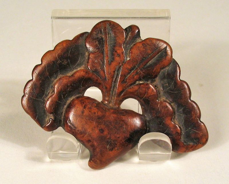 DESCRIPTION: A Chinese peach toggle (guajian) crafted from a flat piece of burl wood with large spreading leaves, representing longevity in Chinese iconography. Two holes on either side of the stem were used for threading a cord from which this toggle would have been suspended as a counterweight to some other object, such as a tobacco pouch. A nice example of Chinese folk art dating from the mid 1800’s or earlier, this toggle is in overall fine condition with aged patina. DIMENSIONS: 1 ½” high (4 cm) x 2” wide (5 cm). 
<div id='rater_target1377094'></div>
