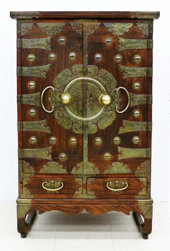 DESCRIPTION:  A tall Korean bandaji chest with elaborately etched brass mounts, having hatchet-shaped hinges on two doors over two lower drawers with brass butterfly mounts. A large flower-shaped center medallion with etched flowering trees dominates the front and contains the locking mechanism (original key included). The two doors open to reveal three small drawers (ideal for jewelry) over three larger drawers with bat-shaped mounts.  The upper portion unlocks to reveal a drop front desk with two drawers and slots for office papers. Latter Choson period (1392–1910), 19th or early 20th century.  DIMENSIONS: 47.5' high 'x 30' wide 'x19'' deep.
<div id='rater_target1383421'></div>
