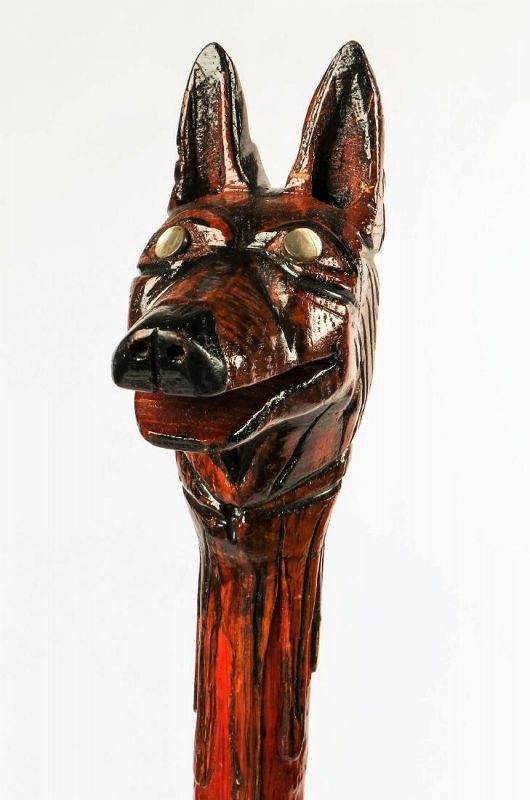 DESCRIPTION: A carved wood cane by Philadelphia carver, Milton Jews (American, b. 1932), with a wolf head grip having abalone eyes, and leaf carvings winding down the shaft of the stick. “J3881” is stamped on the lower shaft near the artist’s stamped name, “Milton Oliver Jews.”  The word “Windy” is carved in bold relief on the opposite lower shaft.  The cane is accented with an aluminum ring toward the neck for attaching a strap or cord to wear the cane over the shoulder, and a rubber cap cushions the bottom tip of the cane. Excellent condition, 20th C. DIMENSIONS: 42.5" L (108 cm). 
<p>ABOUT THE ARTIST: Milton Oliver Jews spent his adult life crafting elaborate walking sticks that embodied the spirit and style of the Philadelphia Black working class.  His work took place in the evenings and on weekends in a narrow, cramped South Philadelphia basement, working with salvaged wood and scraps of materials he would incorporate into his canes. His canes bear witness to the demands of “street style,” and to a time when a cane was the mark of a gentleman. The canes, meant to be slung over the shoulders or cradled in the arm, testify to their use as affirmations of identity. Over the years, metal - salvaged from scrap at Mr. Jews’ longtime workplace - came to play an integral role in his walking sticks, providing both decorative banding and eye-catching details.
<p>While some of his sticks have handles clearly shaped to hold one’s weight, many others do not welcome a hand’s load-bearing grasp, having the horns of a devil’s head, the slender neck of a brass egret, or the spiked ears on a fanciful wolf. Perhaps that’s why Mr. Jews never referred to his canes as “walking sticks.”  His sticks were meant more for carrying than for walking. Hence he attached rings and cords on many of the canes’ shafts that allowed the carrier to slip them over a shoulder and wear them as one would a piece of clothing.  The sticks also filled the added function of protection, a quality not unimportant on the streets of South Philly.  Carried proudly over the shoulder, the walking stick served as both a statement of style as well as a warning.

<div id='rater_target1386488'></div>
