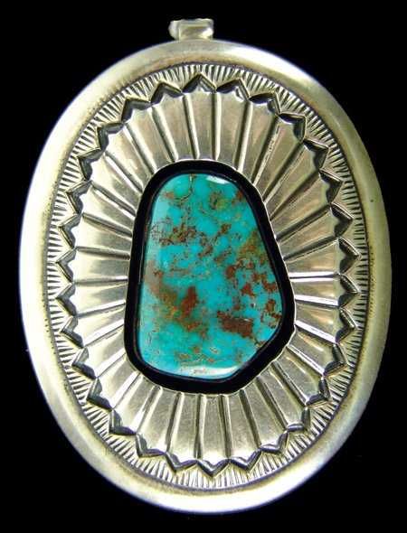 DESCRIPTION:  A fine hand stamped sterling sunburst design pendant with a large, high quality Cerillos mine turquoise stone set in shadowbox style. Reverse is stamped, “E. Bilagody, Sterling.” A Navajo silver artist, Ernest Bilagody is based in Gallup, NM.  Late 1900s, excellent condition. DIMENSIONS: 2-1/4" x 1-5/8"
<div id='rater_target1386639'></div>
