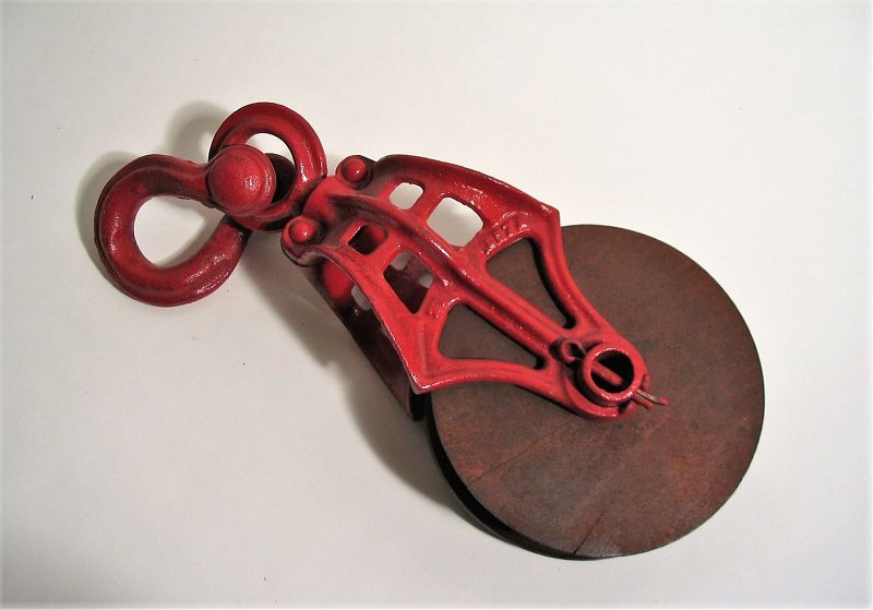 DESCRIPTION:  This wonderful old pulley reflects the beauty of vintage industrial design and today makes a decorative accent in a country, farmhouse or industrial decor. The pulley is a simple machine that, when used with a rope, will reduce the amount of force needed to lift a load. On this pulley, the heavily cast pierced iron shaft and swivel eye are painted red, and are attached with a snatch pin to a grooved wooden wheel. Excellent, workable condition. DIMENSIONS:  13 ¼” long; wheel diameter is 5 ½”.
<div id='rater_target1386911'></div>
