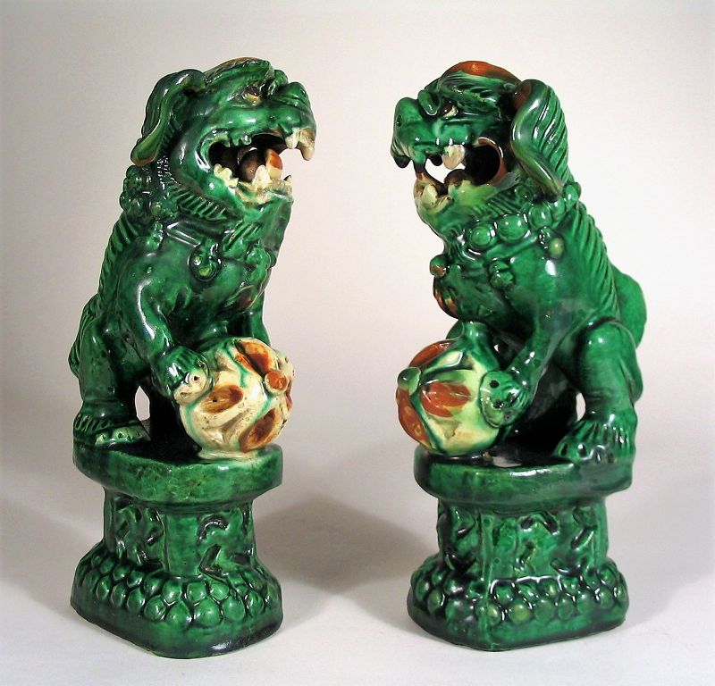 DESCRIPTION: A fierce pair of Chinese pottery foo dogs, early Qing, 18th/19th C., covered with a heavy green glaze and seated on pedestals. Each bares its teeth ferociously while holding a ball between their front paws as well as in their mouths. Good detail with finely ribbed backs and curled manes. Very good condition. DIMENSIONS: Each approximately 9 ½” high (24 cm) x 5” wide (12.7 cm).   

<div id='rater_target1388222'></div>
