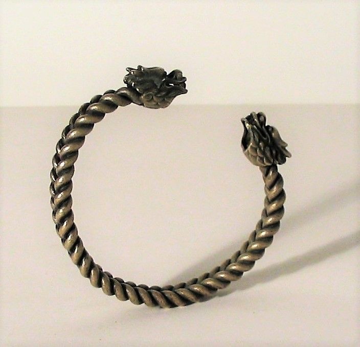 DESCRIPTION:  A Chinese minority tribe antique silver bracelet, handcrafted from two sturdy silver coils, each twisted and joined to form a braided pattern, with each end terminating in a silver, four-horned dragon head. 
The woven coils, simulating the dragons’ bodies, and the gap between the horned heads allow the bracelet to be “sized” to any wrist.  Very decorative and an authentically old piece of tribal jewelry. DIMENSIONS:  3 1/8” exterior diameter (8 cm); 2.5" interior diameter (6.4 cm).

<div id='rater_target1392412'></div>
